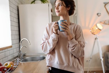 Ev mutfağında kahve içerken pencereden dışarı bakan güzel bir kız.