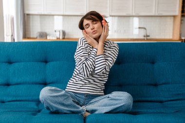 Evdeki kanepede kulaklıkla müzik dinlerken şarkı söyleyen mutlu güzel kız.