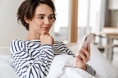 Mutlu güzel kız evde uyuduktan sonra yatarken cep telefonu kullanıyor.