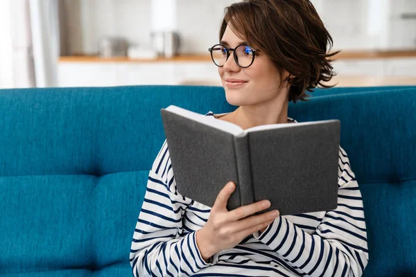 Šťastná Krásná Žena Brýlích Čtení Knihy Zatímco Sedí Gauči Doma — Stock fotografie