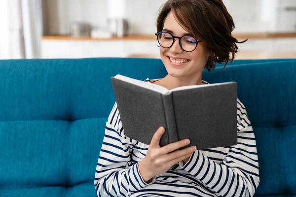 Mulher Bonita Feliz Óculos Livro Leitura Enquanto Sentado Sofá Casa — Fotografia de Stock