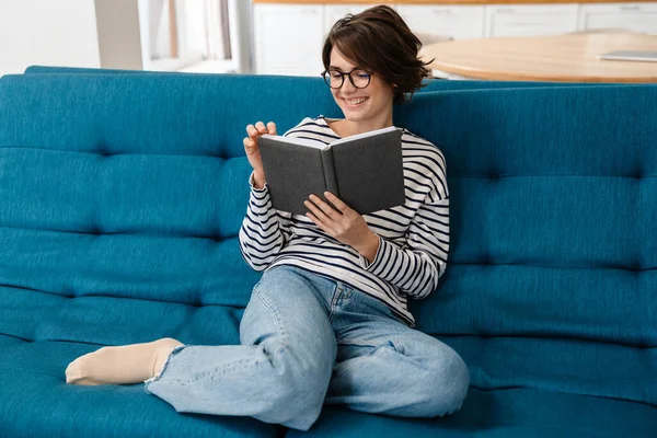 Feliz Hermosa Mujer Gafas Lectura Libro Mientras Está Sentado Sofá —  Fotos de Stock