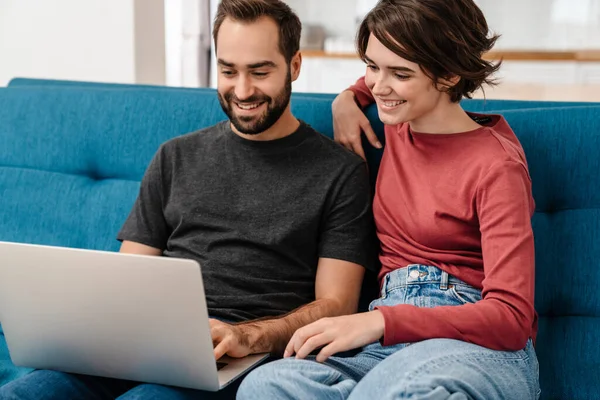 Feliz Joven Pareja Sonriendo Utilizando Ordenador Portátil Mientras Está Sentado —  Fotos de Stock