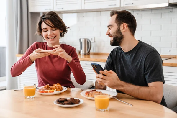 Szczęśliwa Piękna Para Przy Użyciu Telefonów Komórkowych Podczas Śniadania Domu — Zdjęcie stockowe