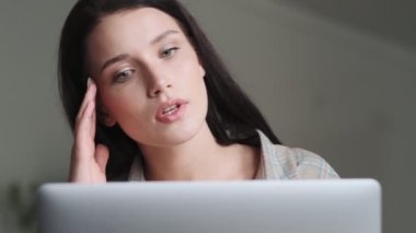 Düşünen, odaklanmış, tişört giyen bir iş kadınının yakın plan görüntüsü ofiste oturan dizüstü bilgisayarını kullanıyor.