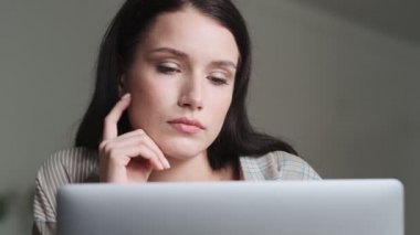 Ciddi bir iş kadını gömleği giyerken yakın plan görüntüsü ofiste oturan dizüstü bilgisayarını kullanıyor.
