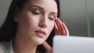 Yorgun bir iş kadınının yakın plan görüntüsü, ofiste dizüstü bilgisayarıyla çalışırken şakaklarına masaj yapıyor.