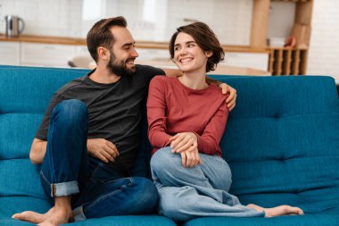 Mutlu genç çift evde televizyon izlerken sarılıp uzaktan kumanda kullanıyor.