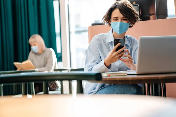 Menina Feliz Máscara Protetora Usando Celular Enquanto Trabalhava Com Laptop — Fotografia de Stock