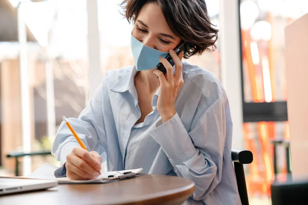 Menina Feliz Máscara Protetora Falando Celular Enquanto Escreve Notas Café — Fotografia de Stock