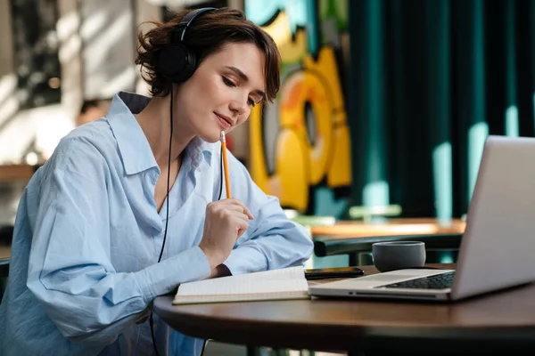 Konzentriertes Mädchen Schreibt Notizen Während Laptop Und Kopfhörer Café Benutzt — Stockfoto