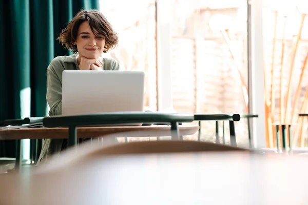 坐在室内咖啡店时 微笑着与笔记本电脑一起工作的高加索女孩 — 图库照片
