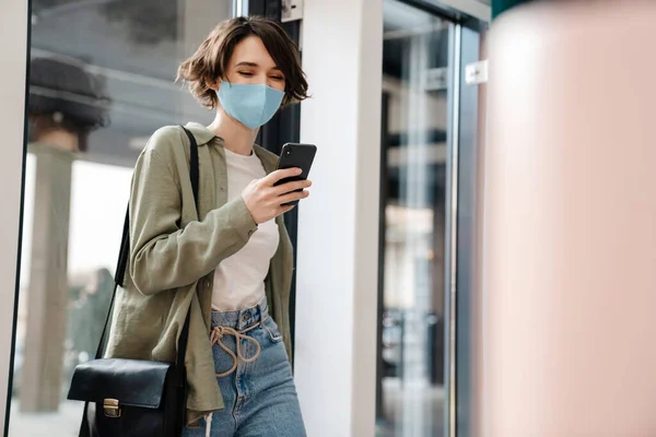 Happy Girl Protective Mask Using Cellphone While Walking Indoors — Stock Photo, Image