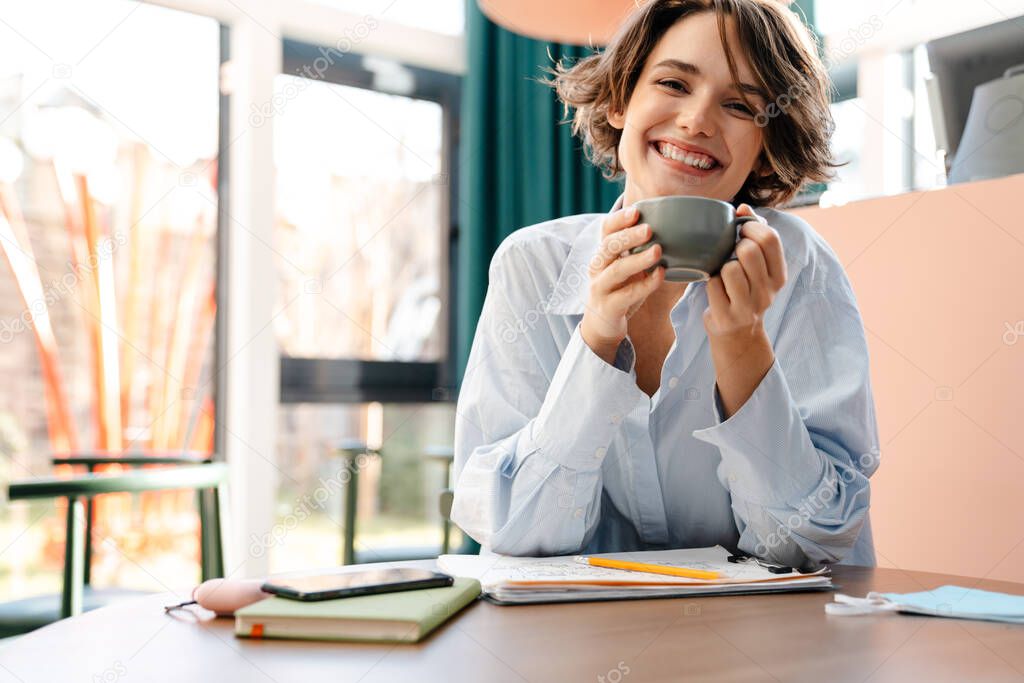 Young smiling attractive lady drinking coffee while ralxing in cafe indoors