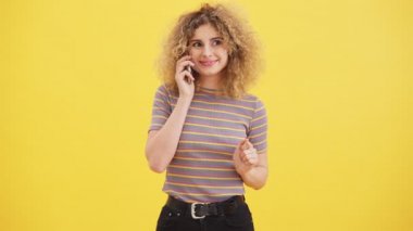 Mutlu, sarışın bir kadın, stüdyodaki sarı duvarın arkasında duran akıllı telefonunu kullanarak birini arıyor.