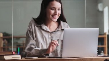 Gülümseyen bir iş kadını ofiste video bağlantısıyla konuşurken dizüstü bilgisayarını kullanıyor.