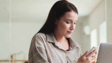 Memnun bir iş kadını ofiste oturan akıllı telefonuyla konuşuyor.