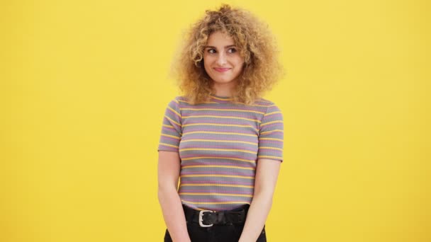 一位面带微笑 卷曲的金发女子正凝视着站在工作室黄色墙壁上的摄像机 — 图库视频影像