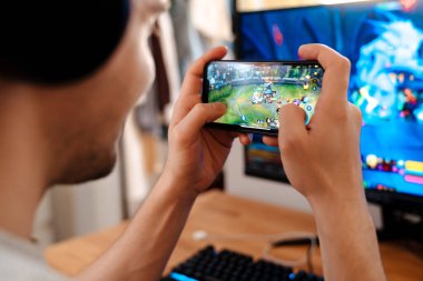 Evde cep telefonuyla video oyunu oynayan traşsız esmer adam.