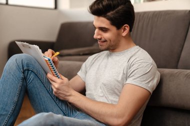 Mutlu esmer adam evde otururken notlar yazıyor.