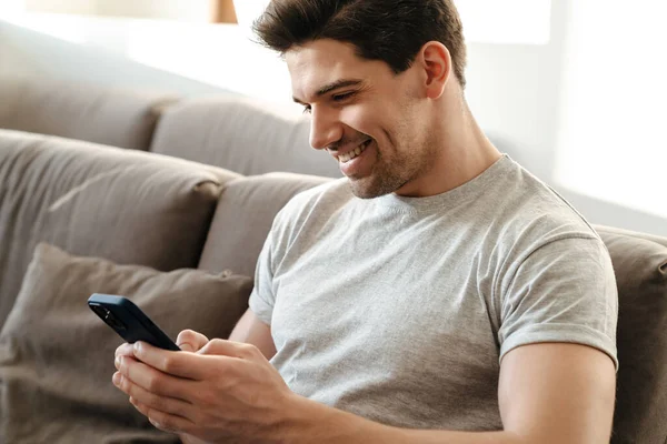 Mutlu yakışıklı genç adam evde dinlenirken cep telefonu kullanıyor.