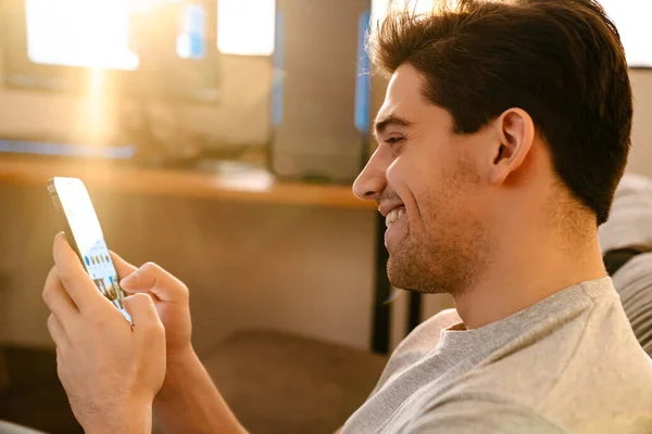 Feliz Morena Chico Sonriendo Utilizando Teléfono Móvil Mientras Descansa Casa — Foto de Stock