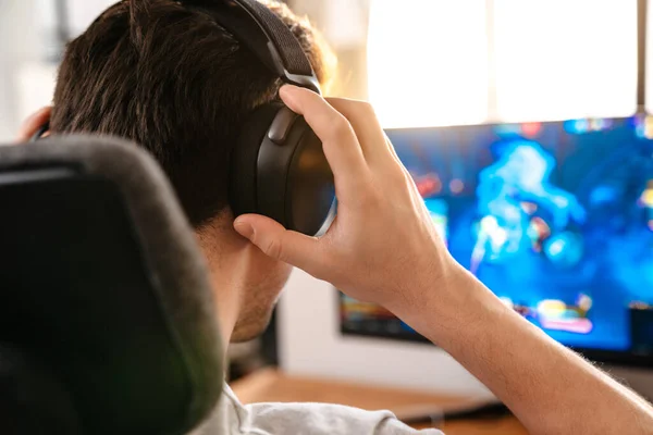白人ブルネット男でヘッドフォン再生ビデオゲームで彼のコンピュータ上で座っている間 — ストック写真