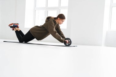 Atletik genç sporcu kadın içeride minder üzerinde çalışırken ekipmanla şınav çekiyor.