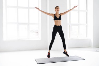 Gülümseyen genç sporcu kadın paspas üzerinde çalışırken atlıyor.