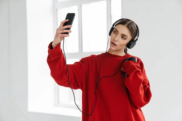 年轻的女运动员戴着耳机 在室内用手机自拍 — 图库照片