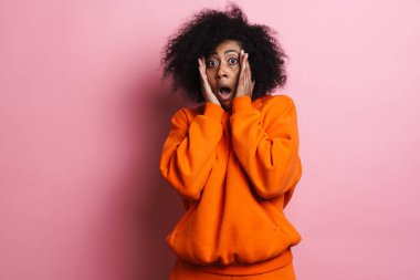 Korkak Afrikalı Amerikalı kadın pembe arka planda izole edilmiş kameraya şok gösteriyor.
