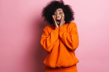 Korkak Afrikalı Amerikalı kadın pembe arka planda izole edilmiş kameraya şok gösteriyor.