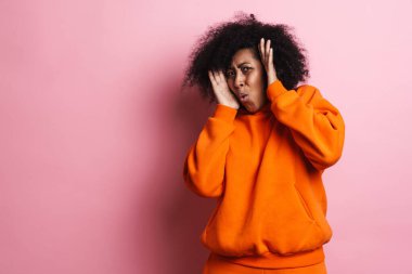 Korkak Afrikalı Amerikalı kadın pembe arka planda izole edilmiş kameraya şok gösteriyor.