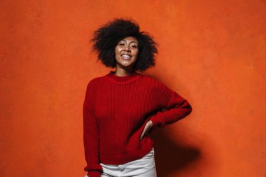 Çekici, gülümseyen, sıradan bir Afrikalı kadın turuncu arka planda tek başına duruyor.