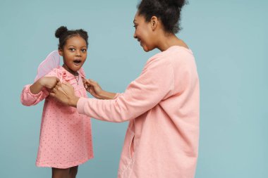 Kelebek kanatlı mutlu siyah anne ve kızı mavi arka planda birlikte eğleniyorlar.