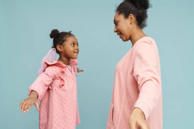 Kelebek kanatlı mutlu siyah anne ve kızı mavi arka planda birlikte eğleniyorlar.