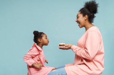 Mutlu siyah anne-kız doğum günü kutlaması mavi arka planda izole edilmiş pastayla