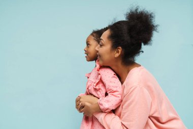 Afrikalı anne ve kız gülümsüyor ve sarılıyorlar mavi duvarın üzerinde.