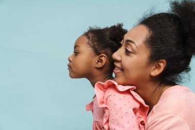 Afrikalı anne ve kız gülümsüyor ve sarılıyorlar mavi duvarın üzerinde.