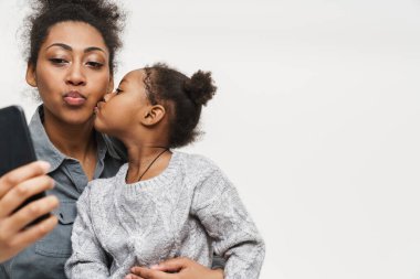 Beyaz duvarda izole edilmiş cep telefonu kullanarak öpüşen Afrikalı anne ve kız.