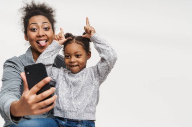 Beyaz duvarın üzerinden izole edilmiş cep telefonu kullanırken Afrikalı anne ve kız dalga geçiyor.