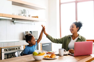 Ev mutfağında kahvaltı yaparken mutlu bir anne ve kız beşlik çakıyor.