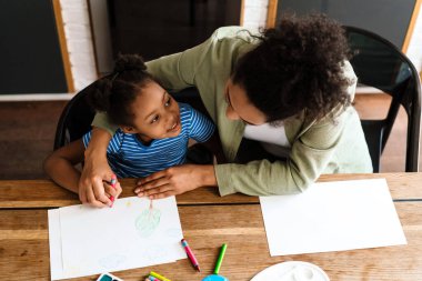 Mutlu bir anne, kızıyla birlikte ev mutfağında resim çizer.