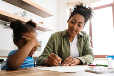 Mutlu bir anne, kızıyla birlikte ev mutfağında resim çizer.