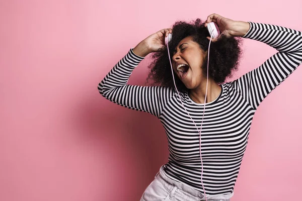 Neşeli Afrikalı Amerikalı kız pembe arka planda izole edilmiş kulaklıklarla dalga geçiyor.