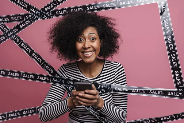 Excited cheerful african woman shopping online with mobile phone, isolated background, sale concept