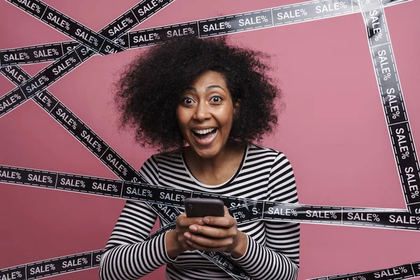 Excited cheerful african woman shopping online with mobile phone, isolated background, sale concept