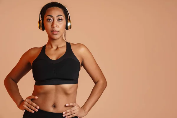 Selbstbewusste Afrikanisch Amerikanische Sportlerin Posiert Drahtlosen Kopfhörern Isoliert Über Beigem — Stockfoto