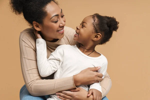 Happy black mother and daughter hugging and smiling isolated over beige background