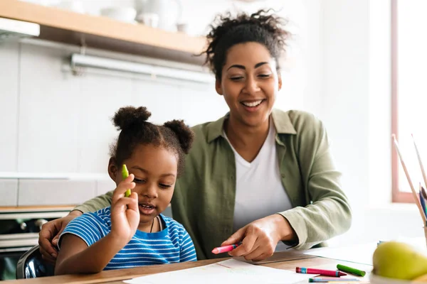 Mutlu bir anne, kızıyla birlikte ev mutfağında resim çizer.